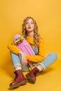 Fashion woman sitting on skateboard on bright yellow background