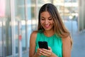 Fashion woman using smartphone standing out the mall. Attractive young woman texting while enjoying a shopping day.