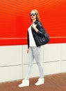 Fashion woman wearing a rock black jacket, sunglasses and bag walking in city over red Royalty Free Stock Photo