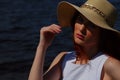 Fashion woman in white dress and glamour hat outdoors on river shore, deep blue water on background. Royalty Free Stock Photo