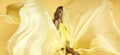 Fashion Woman in Yellow fluttering Dress. Glamour Model is posing in Long Silk Fabric flying on Wind. Elegance Royalty Free Stock Photo