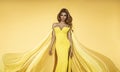 Fashion Woman in Yellow fluttering Dress. Glamour Model is posing in Long Silk Fabric flying on Wind. Elegance Royalty Free Stock Photo