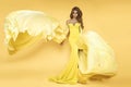 Fashion Woman in Yellow fluttering Dress. Glamour Model is posing in Long Silk Fabric flying on Wind. Elegance Royalty Free Stock Photo