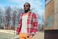 Fashion young african man listens to music in earphones outdoors wearing a plaid red shirt and sunglasses street