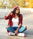 Fashion young african woman having fun in the city park, wearing a red checkered shirt cap sitting Royalty Free Stock Photo