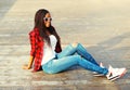 Fashion young african woman sitting in a city park, wearing a red checkered shirt sunglasses Royalty Free Stock Photo