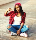 Fashion young african woman sitting is having fun in the city, wearing a red checkered shirt baseball cap Royalty Free Stock Photo