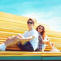 Fashion young couple sits on the bench city park at sunny summer day