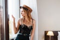 Fashion. A young slender blonde Woman in black clothes and a brown hat, posing looking in anticipation at the window. Close up Royalty Free Stock Photo