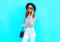 Fashion young smiling woman is talking on a smartphone wearing a black hat and handbag clutch over colorful blue background Royalty Free Stock Photo
