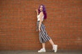 Fashion young woman in stylish clothes. sunglasses, striped pants and white sneakers. walks near a brick wall in the city.