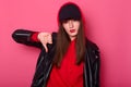 Fashion young woman uses bright red lipstick, wears stylish shirt, leather jacket and black cap. Cheeky tenager shows finger down Royalty Free Stock Photo