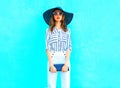 Fashion young woman wearing a straw hat, white pants with a handbag clutch over colorful blue background posing in city Royalty Free Stock Photo
