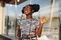 Fashionable African American woman in sunglasses, with shopping bags looking at a shop window in the city Royalty Free Stock Photo