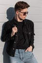 Fashionable American young hipster man in vintage sunglasses in youth stylish casual denim clothes with backpack is rests near Royalty Free Stock Photo