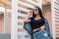 Fashionable american young hipster woman in a stylish black top in a vintage denim jacket in a trendy skirt is resting Royalty Free Stock Photo
