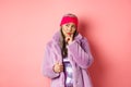 Fashionable asian senior woman looking doubtful, thinking and frowning indecisive, standing in purple faux fur coat and