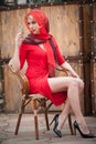 Fashionable attractive blonde woman in red dress sitting on chair. Beautiful elegant woman with red scarf posing in elegant scene Royalty Free Stock Photo