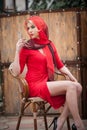 Fashionable attractive blonde woman in red dress sitting on chair. Beautiful elegant woman with red scarf posing in elegant scene Royalty Free Stock Photo