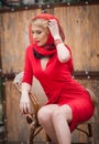 Fashionable attractive blonde woman in red dress sitting on chair. Beautiful elegant woman with red scarf posing in elegant scene Royalty Free Stock Photo