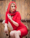 Fashionable attractive blonde woman in red dress sitting on chair. Beautiful elegant woman with red scarf posing in elegant scene Royalty Free Stock Photo