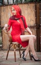 Fashionable attractive blonde woman in red dress sitting on chair. Beautiful elegant woman with red scarf posing in elegant scene Royalty Free Stock Photo