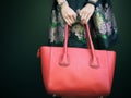 Fashionable beautiful big red handbag on the arm of the girl in a fashionable black dress, posing near the black wall on a warm su