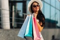 Fashionable happy woman, in a dress and black glasses, with shopping bags near a shopping center on Black Friday