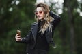 Fashionable beautiful and sensual blonde model girl in black leather jacket, in jeans and it stylish sunglasses takes a Royalty Free Stock Photo