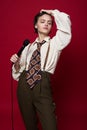 Fashionable beautiful singer girl in retro coat, tie and pants with microphone in hands posing on red background. Royalty Free Stock Photo