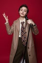 Fashionable beautiful singer girl in retro coat, tie and pants with microphone in hands posing on red background. Royalty Free Stock Photo