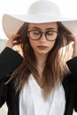 Fashionable beautiful young business woman with glasses in a white hat and a black jacket on the street. Stylish pretty girl in Royalty Free Stock Photo