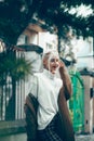 Fashionable beautiful young woman with blond hair in a stylish long coat, checkered pants and glasses poses in the city Royalty Free Stock Photo