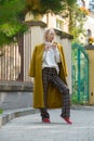 Fashionable beautiful young woman with blond hair in a stylish long coat, checkered pants, red shoes and glasses poses Royalty Free Stock Photo