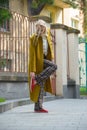 Fashionable beautiful young woman with blond hair in a stylish long coat, checkered pants, red shoes and glasses poses Royalty Free Stock Photo