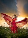 Fashionable beautiful young woman in long red dress posing outdoor with cloudy dramatic sky in background. Attractive brunette Royalty Free Stock Photo