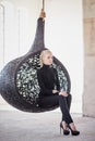 Fashionable blond woman sits on a round chair.