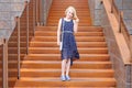 Fashionable blonde girl in preteen age in a dress standing on a stylish rusty staircase in a modern building