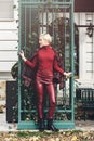 fashionable blonde girl with a red lipstick posing outdoors . Dressed in a red leather leggings, turtleneck and Royalty Free Stock Photo