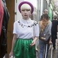 Fashionable blonde in white vintage blouse, green skirt and burgundy hat is on Columbia Road