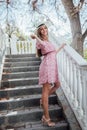 beautiful fashionable blonde woman in a hat and pink dress on the stairs