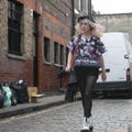 Fashionable blonde woman in in multi-colored blouse, black tights, shorts and a purple hat is on Columbia Road. Street fashion