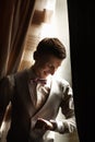 The fashionable bridegroom expects the bride near the window. Portrait of the groom in a grey vest