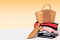 A fashionable brown luxury oak cork women`s handbag on a pile of folded women`s clothing and a single shoe on the table over lig Royalty Free Stock Photo