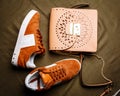 Brown suede sneakers with white accents on a white sole and a brown leather bag with a golden lock on a green woven background Royalty Free Stock Photo