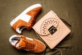 Brown suede sneakers with white accents on a white sole and a brown leather bag with a golden lock on a green woven background Royalty Free Stock Photo