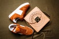 Brown suede sneakers with white accents on a white sole and a brown leather bag with a golden lock on a green woven background Royalty Free Stock Photo