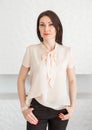 Fashionable brunette girl in a light blouse stands against a white wall, posing and looking at the camera Royalty Free Stock Photo