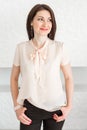 Fashionable brunette girl in a light blouse stands against a white wall, posing and looking at the camera Royalty Free Stock Photo