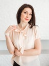 Fashionable brunette girl in a light blouse stands against a white wall, posing and looking at the camera Royalty Free Stock Photo